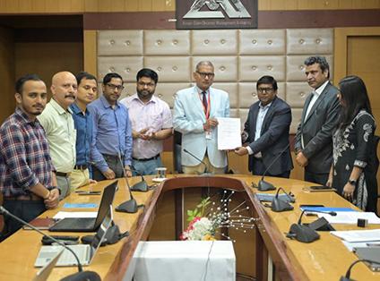 The participants in the contract signing stand around a conference table.